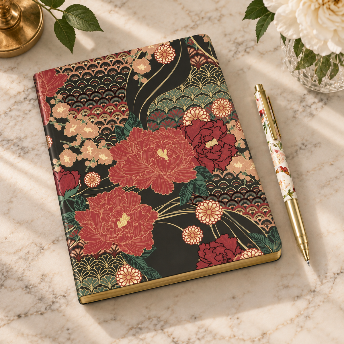 Floral hardcover journal with gold-edged pages and decorative pen on marble surface