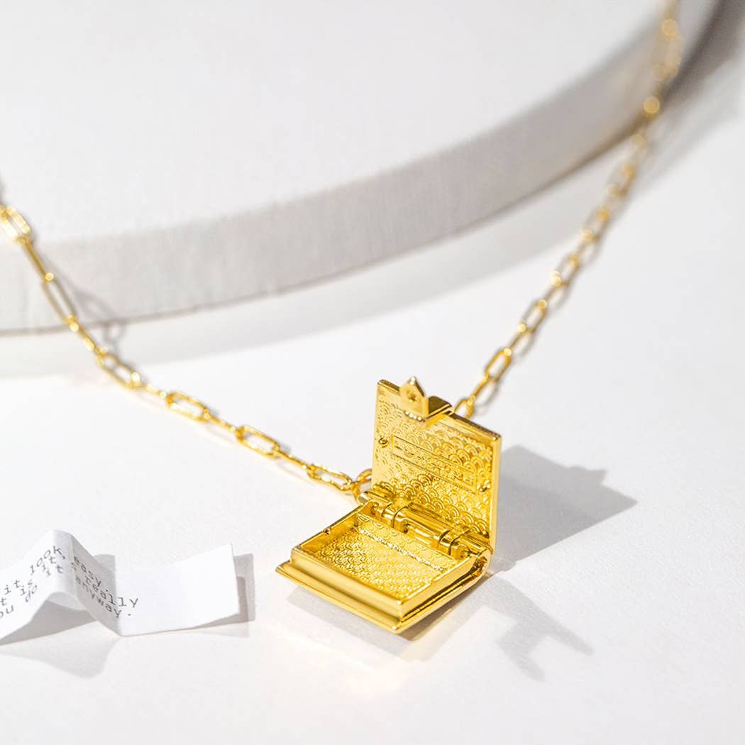 Gold necklace with an open book pendant on a white background