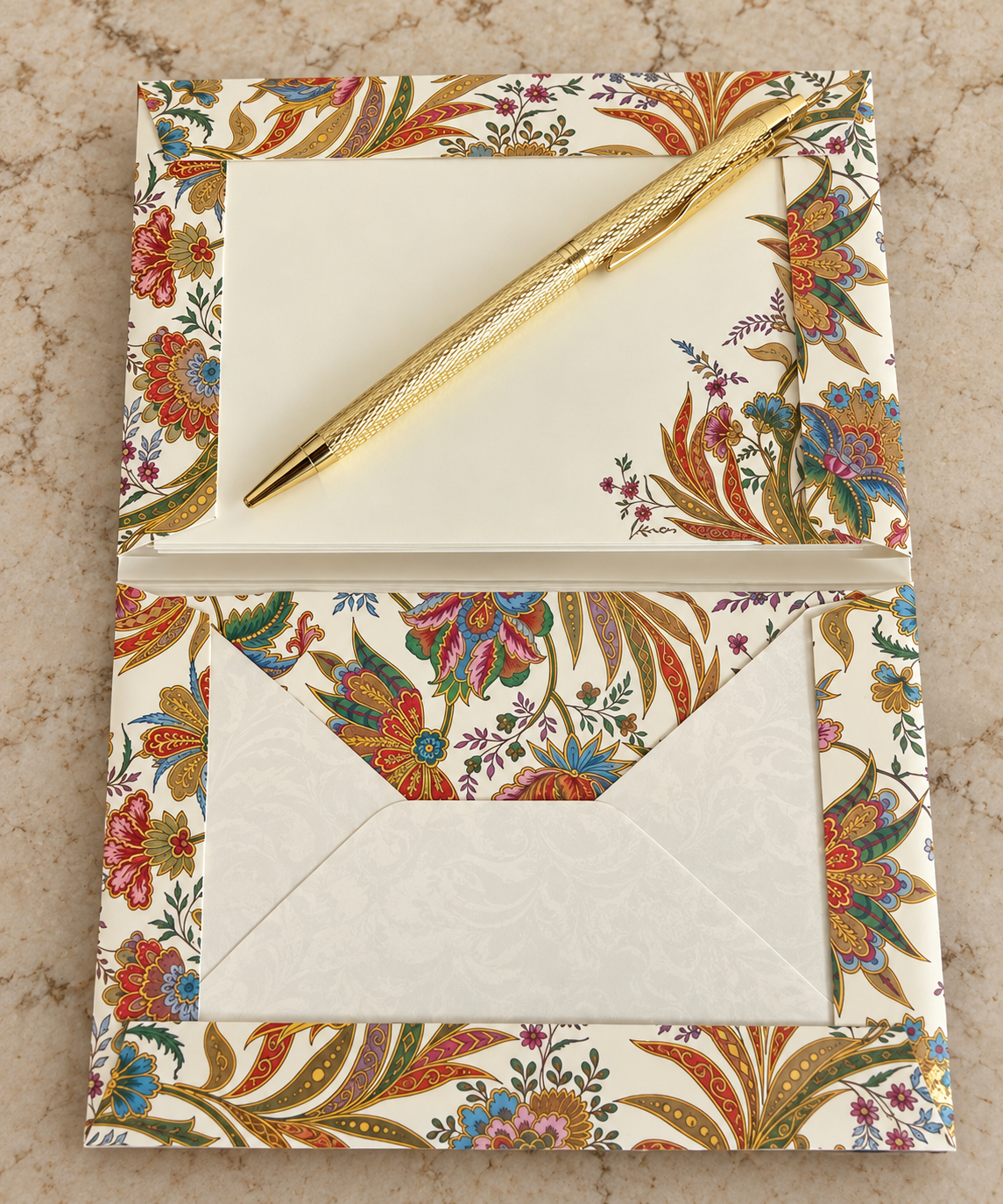 A floral-patterned stationery set featuring a matching envelope, card, and notepad with a gold pen resting on top, displayed on a textured beige surface.