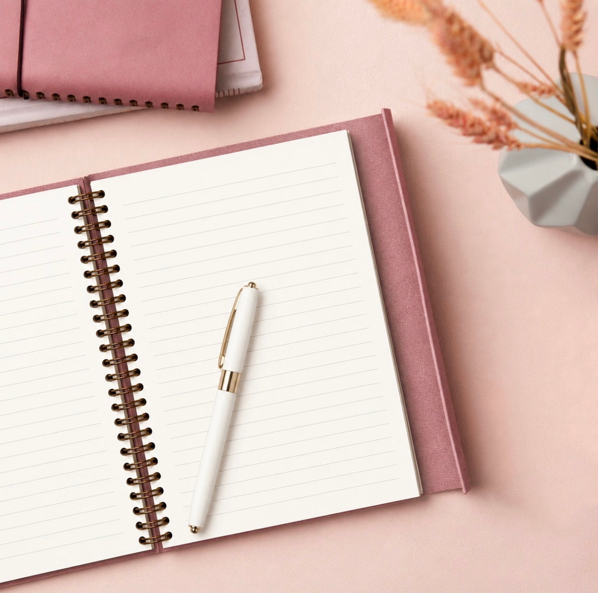 Open dusty rose journal with lined pages and white pen with gold detailing