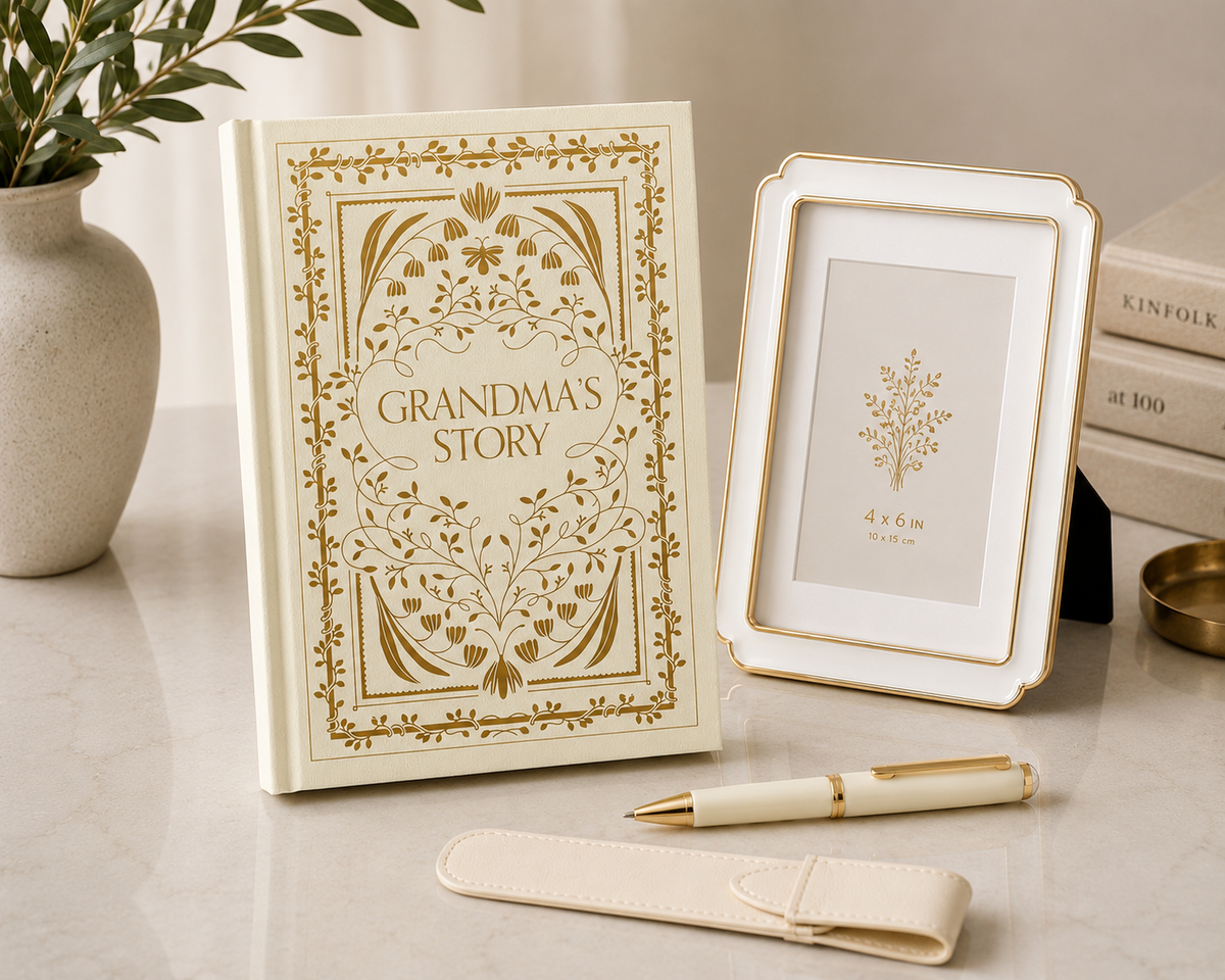 Grandma’s Story keepsake book with gold detailing, framed photo, white and gold pen, and leather pen holder styled on a neutral tabletop.