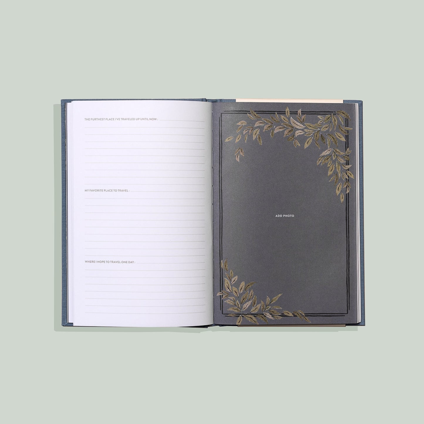 Open blue travel journal showing lined writing prompts on one page and a decorative photo page with gold botanical accents and space to add a photo.