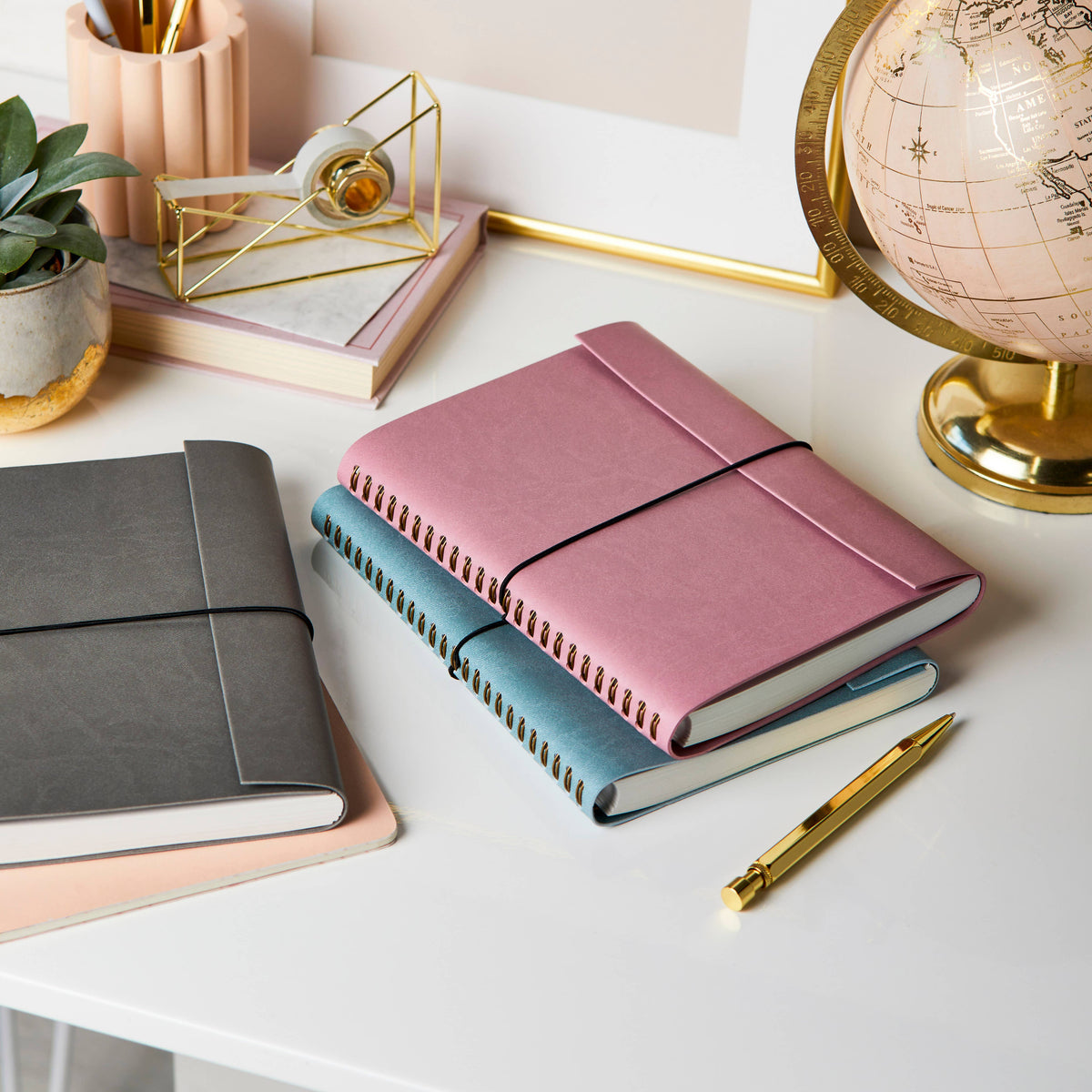 Light grey and dusty rose journals with gold pen on a white desk